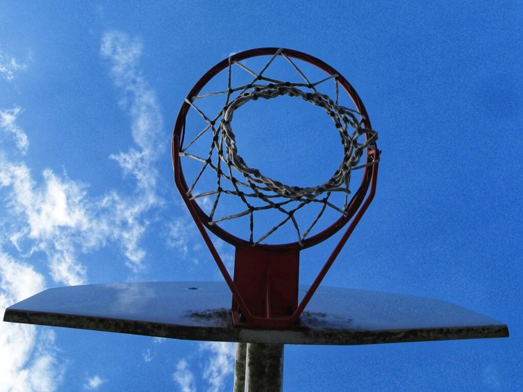 An image of a basketball goal from directly under the net. The blue sky and some wispy, white clouds are visible behind the goal.